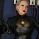 Nahaufnahme von Domina Herrin Xena in schwarzem Lederkorsett und Lederjacke mit goldener Brosche, eine Peitsche in der Hand.
