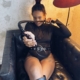 Bizarrlady Kiki Reyna sitzt in schwarzem Outfit und Stiefeln in einem Chesterfield-Ledersessel und hält eine geflochtene Peitsche.